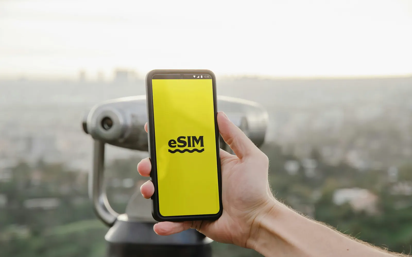 A hand holding a phone displaying an eSIM activation screen, overlooking a city from a viewpoint