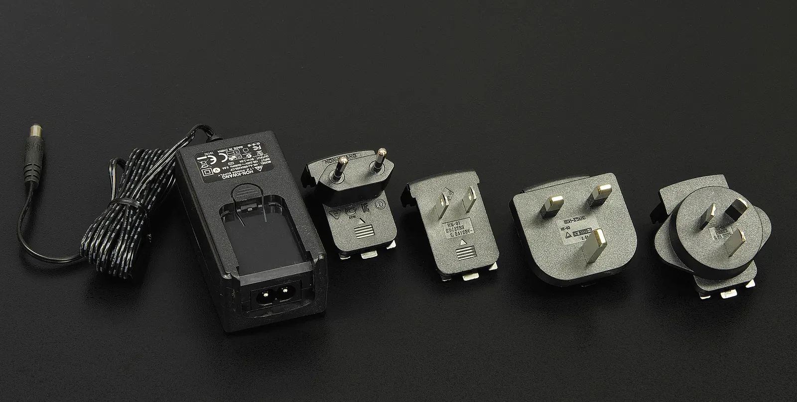 A set of universal travel plug adapters and a power charger on a dark surface