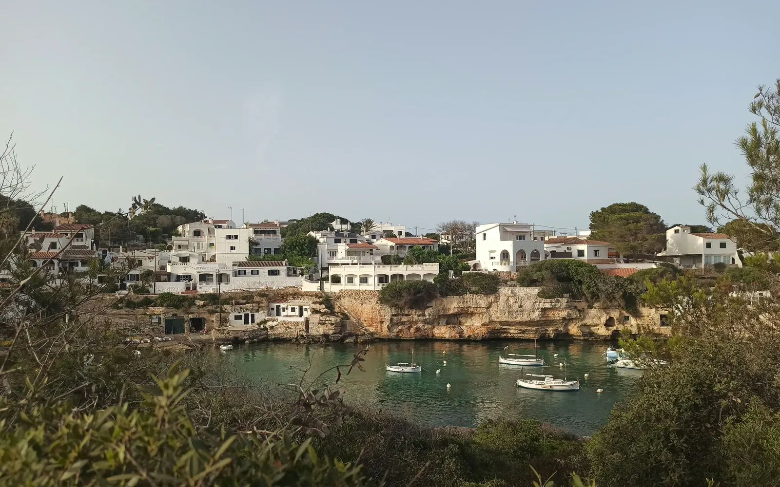 A quiet harbor village of white Mediterranean houses overlooking a small bay of moored fishing boats